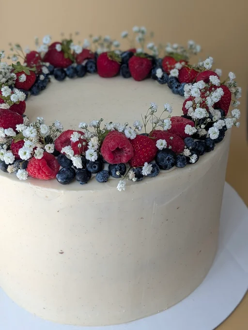 A clean white wedding cake with a ring of berries and flowers